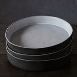 Stack of three white Eco Gres bowls with matte gray exteriors viewed from above on dark wooden surface
