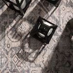 Top-down close-up of rug texture with a black lantern casting shadows onto flat woven polyester surface
