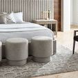 Three Reyes Ottomans arranged side-by-side at the foot of a bed on a patterned rug in a bedroom setting
