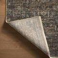 Corner of the rug lifted to reveal the light-colored woven backing and finished edge