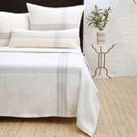 Geneva Blanket in muted plaid pattern with soft combed cotton draped over bed with pillows and side table