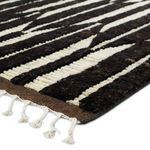 Close-up showing ribbed texture of dark brown and ivory wool pile and white knotted fringe