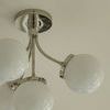 Close-up bottom-side view showing polished metal arms and spherical frosted glass shades against ceiling