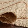 Rug edge partially rolled to reveal thick woven jute texture and braided detailing