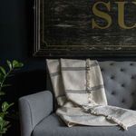 50x70 inch cotton throw in cream with subtle black horizontal stripes and fringed edges draped over gray sofa