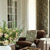 Brass picture light installed high on planked wall in a living room with floral arrangement and brown armchair