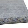 Rug edge rolled up displaying pile texture and color gradient from blue to gray with intricate design