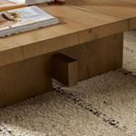 Close-up of bottom wood block leg resting on carpet with table top edge and wood grain visible