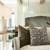 Olive velvet pillow styled on beige sofa paired with a gray and black patterned pillow and a nearby table lamp