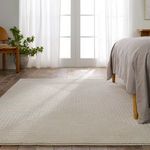 Cream geometric rug placed in bright bedroom with bed legs, potted plant, and sheer curtains