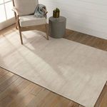 Rug placed on wood floor with beige armchair and small concrete side table in sunlit room