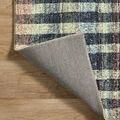 Corner flipped back exposing gray fabric backing and stitched edge on multi rug