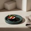 Green marble tray used as a base with a small bowl holding tomatoes and mozzarella, styled with a knife and cloth