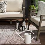 Rug under beige sofa and chair on outdoor deck with black lanterns and white watering can near gray cushion chair