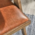 Close-up of Dolton Arm Chair’s leather seat and wooden frame resting on textured rug and floor