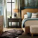 Side view of bed styled in a rustic bedroom with wood dresser, window, and blue-green accent pillows