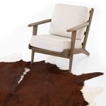 Light beige cushioned wooden armchair positioned on brown and white cowhide rug against white background