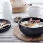 Pacifica bowl filled with cereal and figs, side angle on wooden coaster with table setting background