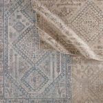 Rug partially folded back revealing front and back sides with muted blue and beige colors