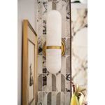 Salon sconce with gold finish mounted on decorative stone tile wall near framed art and flowers