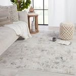 Rug styled in a light-filled living room with beige sofa, knit throw, wooden side table, and pouf