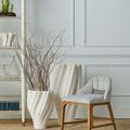 Vases displayed in a room setting next to a gray upholstered chair and decorative branch accents inside smaller vase