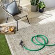 Taupe and charcoal rug displayed outdoors with woven chair, green hose, and potted plants