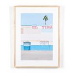 Framed photograph of a building facade with blue and white walls, pink signage, and a single palm tree