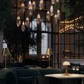 Two brass lamps on a dark green velvet couch setting with hanging crystal pendant lights overhead