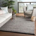 Rug laid out on wood porch floor styled with gray wicker outdoor sofa and chair with patterned pillows.