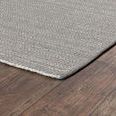 Side view of rug lying flat on dark hardwood floor revealing thin profile