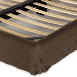 Corner detail of bed showing brown linen slipcover with stitched pleat and wooden slats under mattress