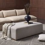 Side angle of ottoman highlighting fabric texture and continuous wood base