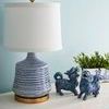 Console table with blue and white textured lamp, blue ceramic foo dog figurines, and green plant on a blue wall