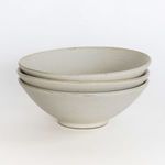 Stack of three creamy stoneware bowls showing shaping and texture variation on white surface