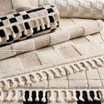 Rolled and folded cream and tan rugs layered with other patterned rugs showing texture and fringe