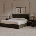 Side angled room view of Sebastion Storage Bed with surrounding black furniture and beige carpet