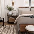 Bedroom side view with rug enhancing warm wooden bed frame and layered textured bedding.
