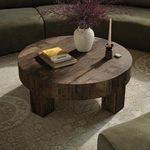 Round coffee table styled in a living room setting with books, vase, candle, surrounded by green sectional sofa