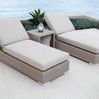 two chaises with light gray cushions in outdoor patio setting by water, side table with lantern between