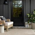 Beige woven rug placed outdoors on stone floor next to wicker armchair and black door