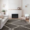 Charcoal and beige rug placed in a minimalist living room with white sofa, wooden chair, and fireplace