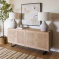 Rug placed under light wood buffet with woven doors and twin concrete lamps with artwork.