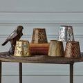 Another view of six assorted chandelier shades on a table, featuring bird and leaf designs in multiple finishes