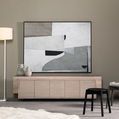 Framed painting displayed on light wood cabinet in modern room with lamp and black stools