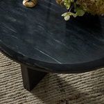Black marble coffee table placed on textured light rug with floral decor and candles on top