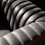 Close-up side angle highlighting channel tufting pattern on arm and back under dramatic light