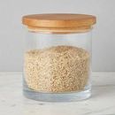 Close-up front view of a large natural wood top canister filled with rice on a marble surface