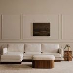 Wider living room view with Sonny ottoman centered on carpet under muted wall painting and white sectional sofa