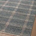 Angled view of rug edge on wood floor showing flatweave texture and blue beige plaid